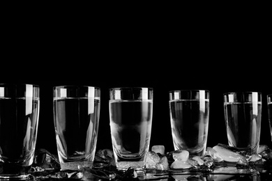 Photo of Vodka in shot glasses and ice on black background