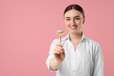 Cosmetologist with facial roller on pink background, space for text