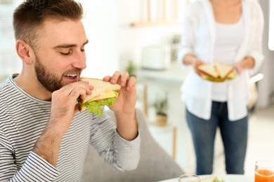 Young man having breakfast with sandwiches in kitchen, space for text