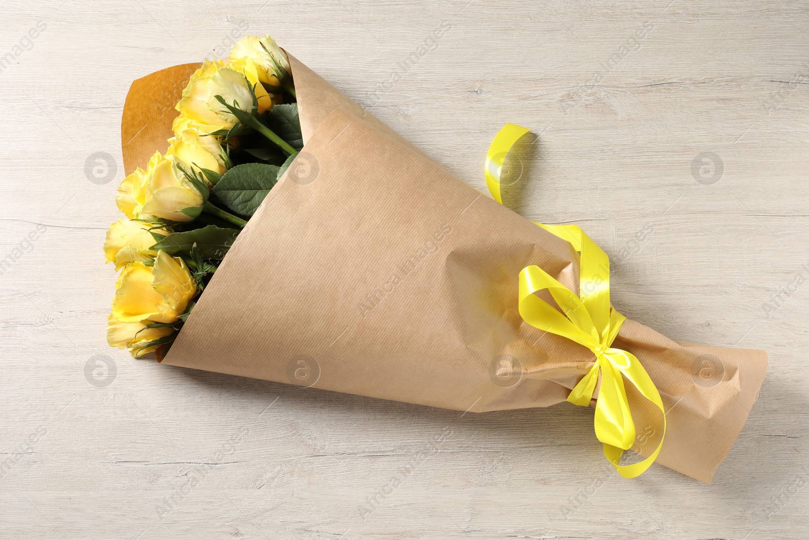 Photo of Beautiful bouquet of yellow roses with ribbon on wooden table, top view