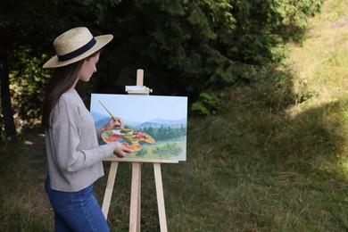 Photo of Young woman drawing on easel outdoors, space for text