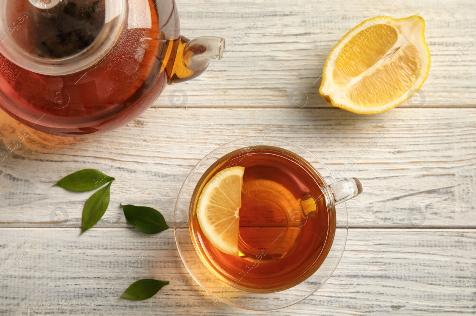 Photo of Glass cup and teapot with black tea on wooden table, top view