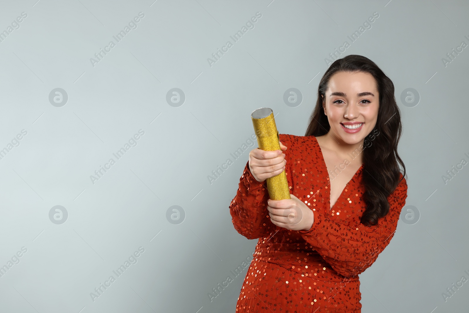 Photo of Young woman blowing up party popper on light grey background, space for text