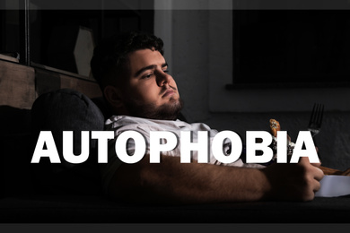 Image of Depressed overweight man eating sweets on sofa at night. Autophobia - fear of isolation