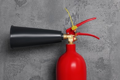 Red fire extinguisher near grey wall, closeup