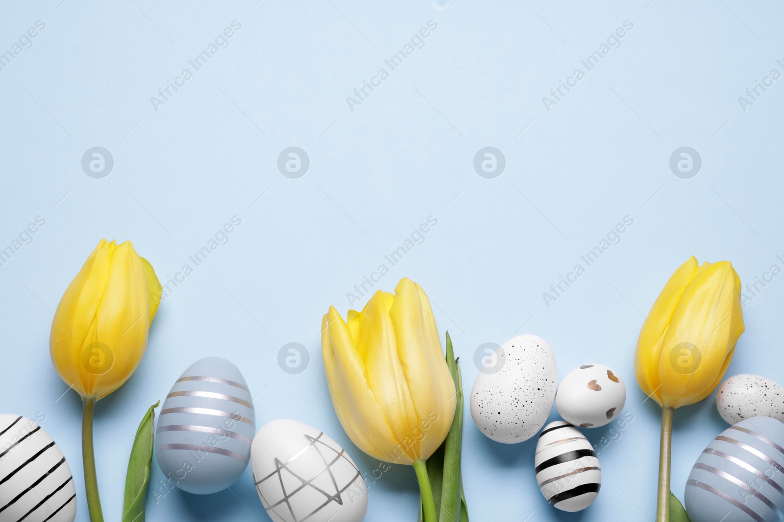 Photo of Flat lay composition with tulips and beautifully painted eggs on light blue background, space for text. Easter celebration