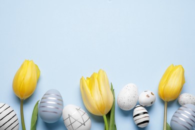 Flat lay composition with tulips and beautifully painted eggs on light blue background, space for text. Easter celebration