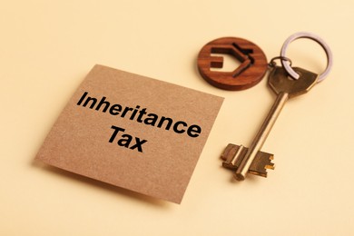 Photo of Inheritance Tax. Card and key with key chain in shape of house on beige background, closeup