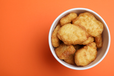 Photo of Bucket with delicious chicken nuggets on orange background, top view. Space for text