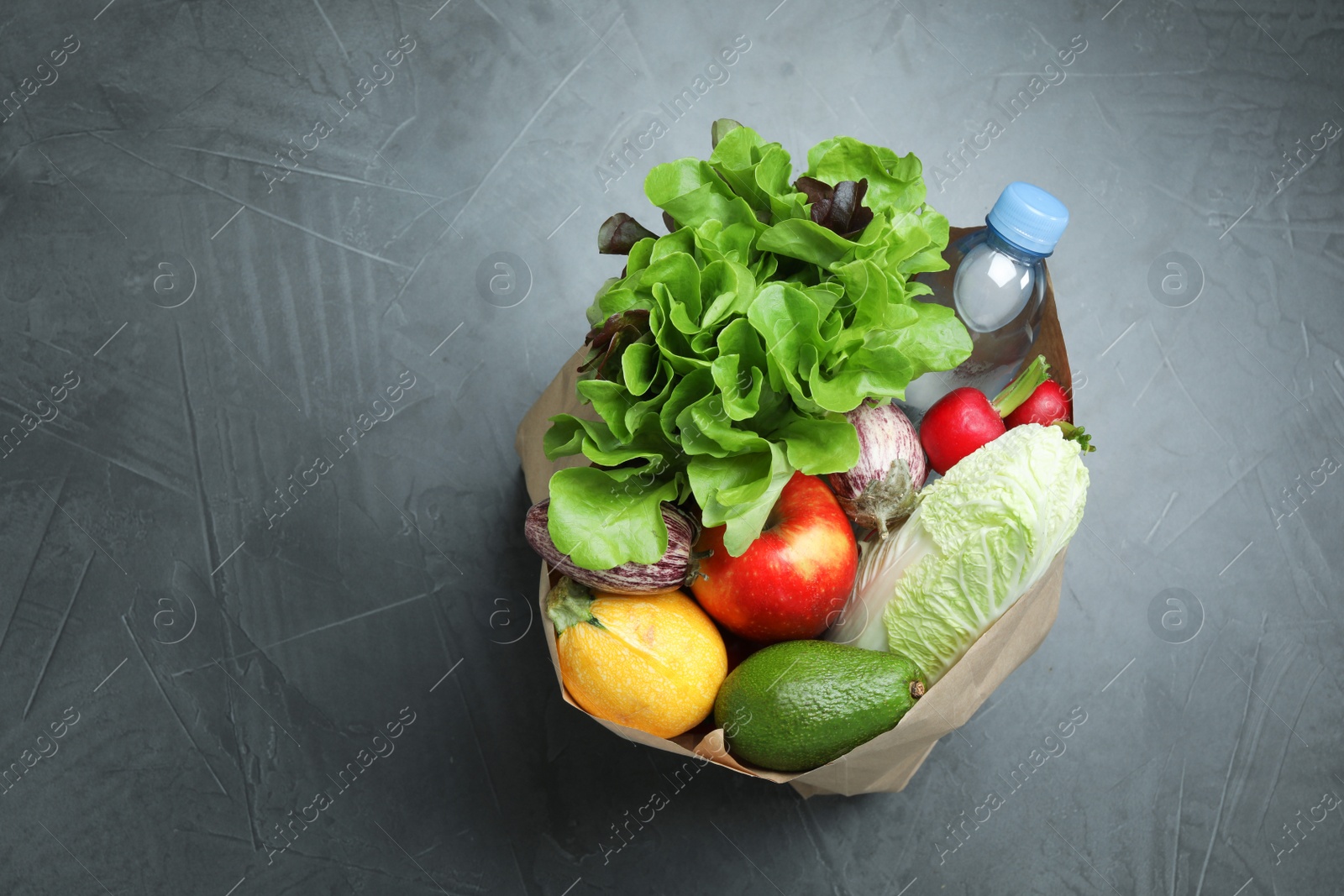 Photo of Paper package full of fresh vegetables and fruits on dark background, top view