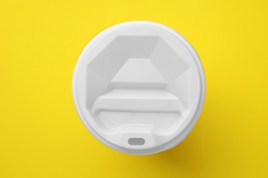 Photo of One paper cup with white lid on yellow background, top view. Coffee to go