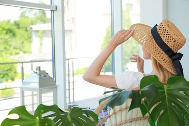 Photo of Woman with straw hat sitting in armchair at indoor terrace