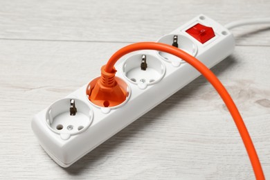 Photo of Power strip with extension cord on white wooden floor, closeup. Electrician's equipment