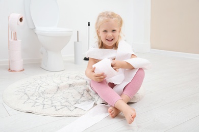 Cute little girl playing with toilet paper in bathroom