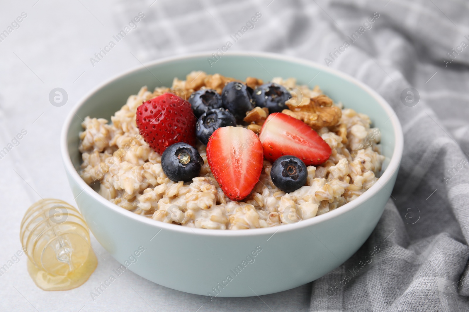 Photo of Tasty oatmeal with strawberries, blueberries and walnuts in bowl on grey table