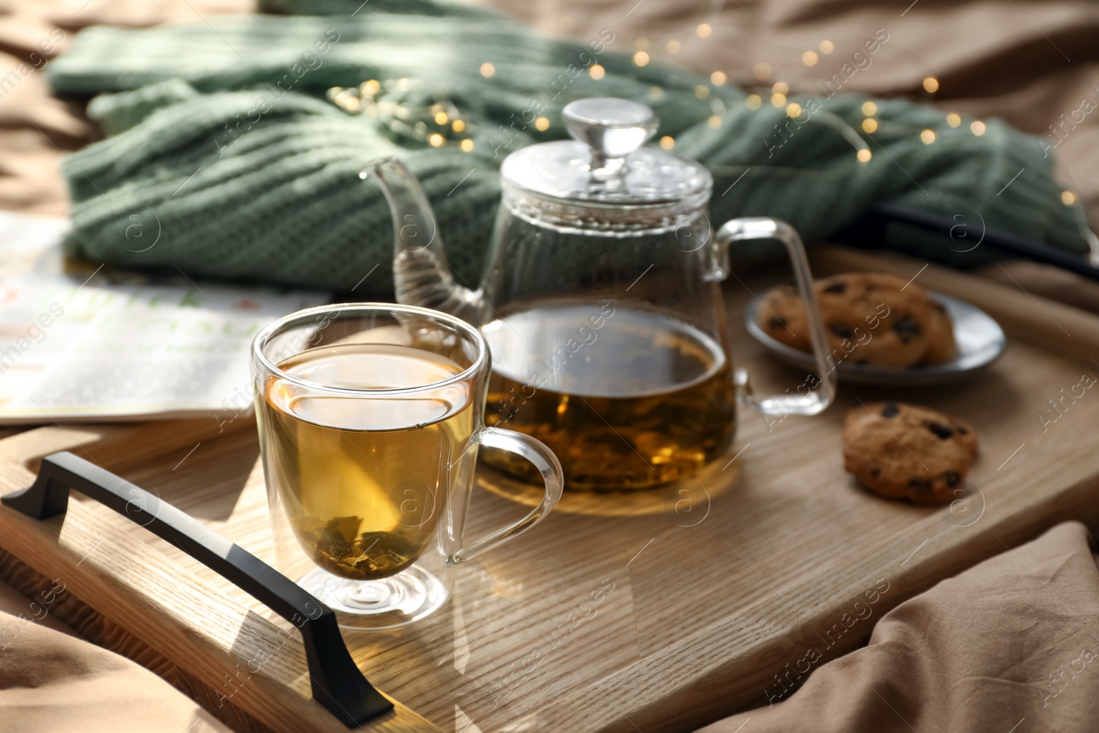 Photo of Wooden tray with freshly brewed tea and cookies on bed in room. Cozy home atmosphere