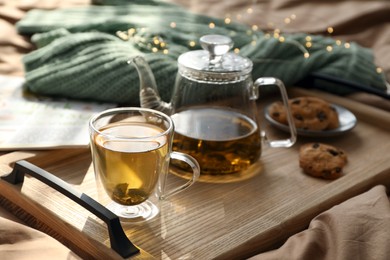 Wooden tray with freshly brewed tea and cookies on bed in room. Cozy home atmosphere