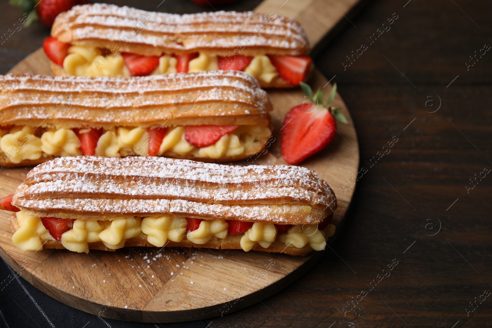 Photo of Delicious eclairs filled with cream and strawberries on wooden table