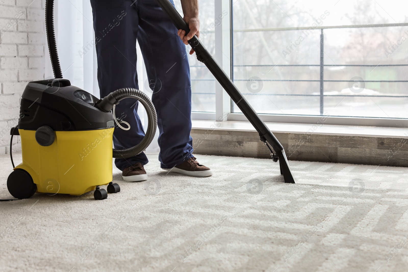 Photo of Male worker cleaning carpet with vacuum indoors