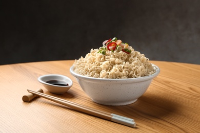 Bowl of hot noodles with vegetables and chopsticks served on table