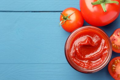 Photo of Jar of tasty ketchup and tomatoes on blue wooden table, flat lay. Space for text