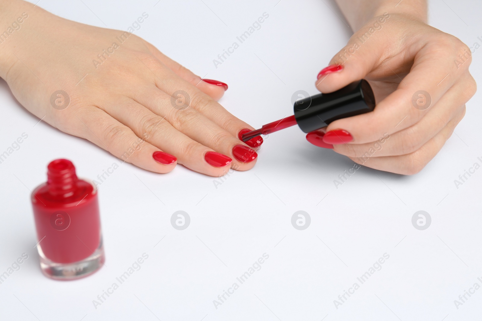 Photo of Woman painting nails with red polish on white background, closeup