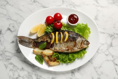 Tasty homemade roasted crucian carp with garnish on white marble table, top view. River fish