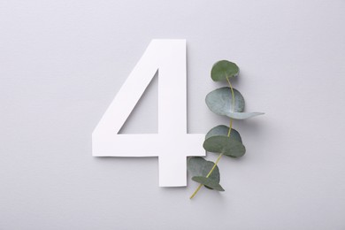 Paper number 4 and eucalyptus branch on light grey background, top view