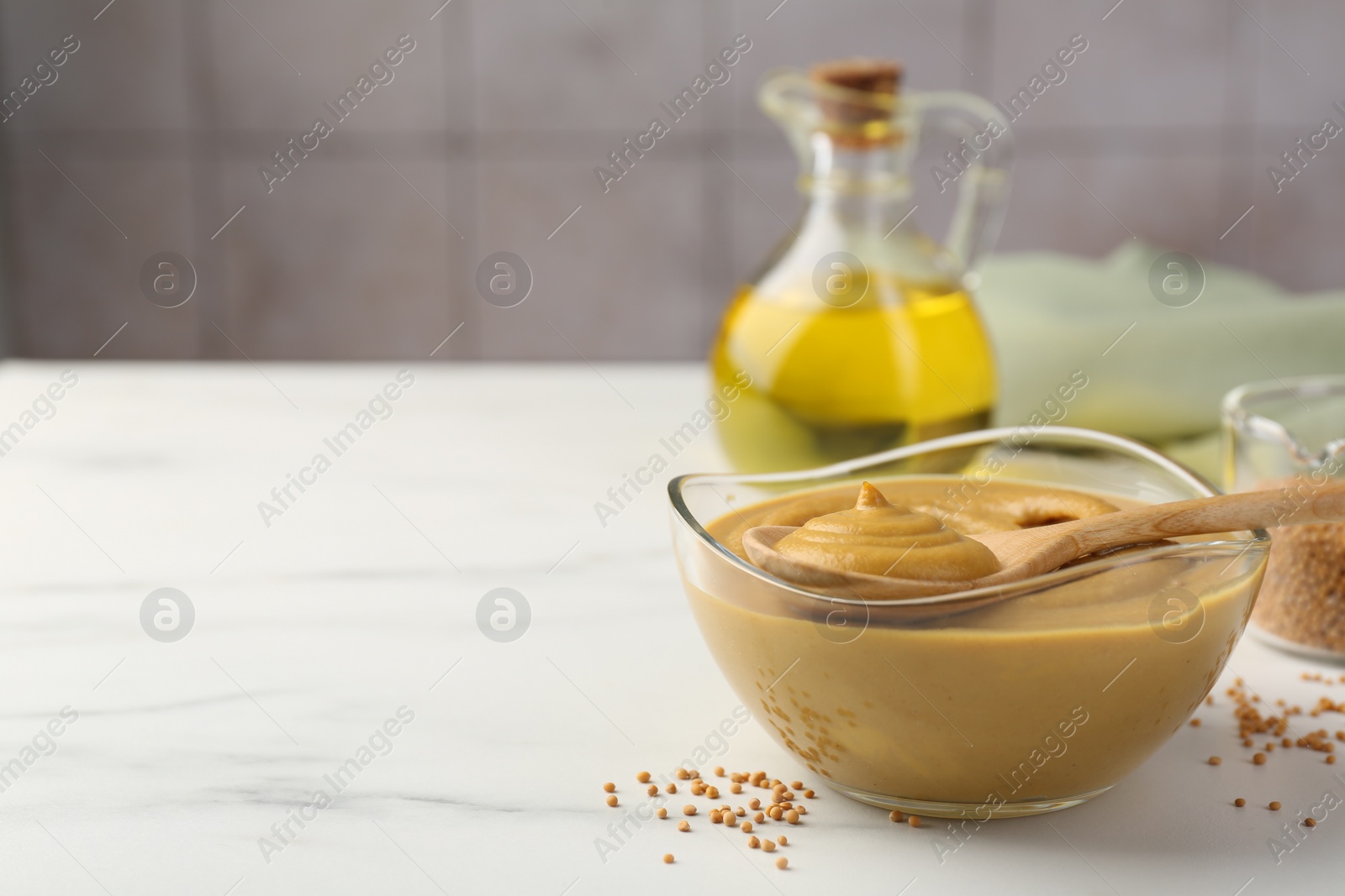 Photo of Spoon and glass bowl with tasty mustard sauce on white marble table, space for text