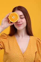 Photo of Beautiful woman covering eye with half of orange on yellow background
