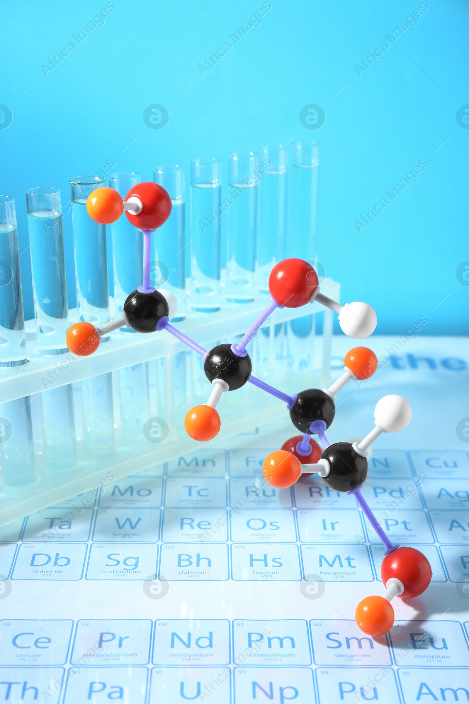 Photo of Molecular model and test tubes on periodic table against light blue background