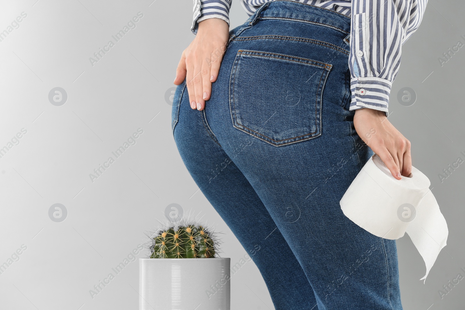 Photo of Woman with toilet paper sitting down on cactus against light grey background, closeup. Hemorrhoid concept