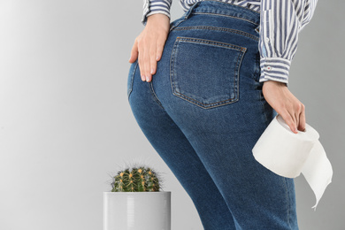 Woman with toilet paper sitting down on cactus against light grey background, closeup. Hemorrhoid concept