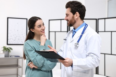 Photo of Doctor with clipboard consulting patient during appointment in clinic