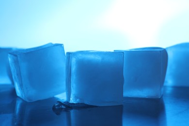 Photo of Crystal clear ice cubes on light blue background, closeup. Color tone effect