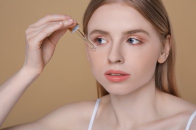 Photo of Woman applying essential oil onto face on light brown background