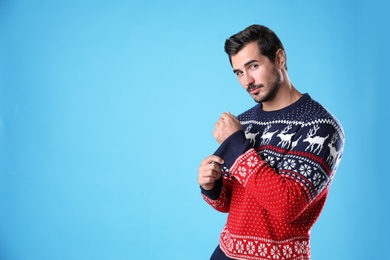 Portrait of happy young man in Christmas sweater on light blue background. Space for text