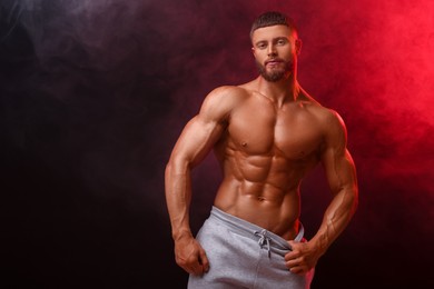 Photo of Young bodybuilder with muscular body in smoke on color background, space for text
