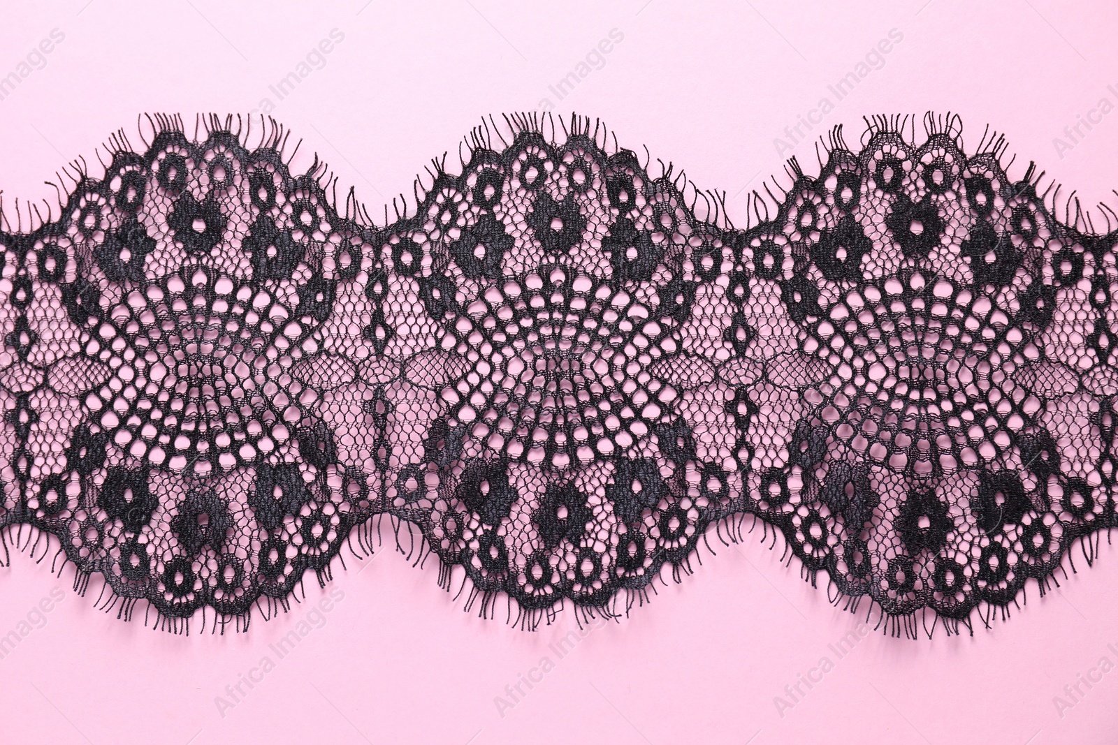 Photo of Black lace on pink background, top view