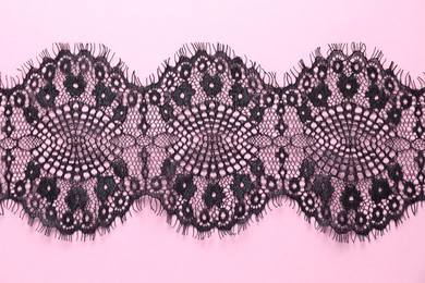 Photo of Black lace on pink background, top view