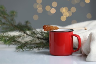 Stick with sugar crystals and cup of drink on white table against blurred festive lights, space for text