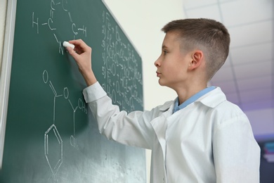 Schoolboy writing chemistry formula on blackboard in class