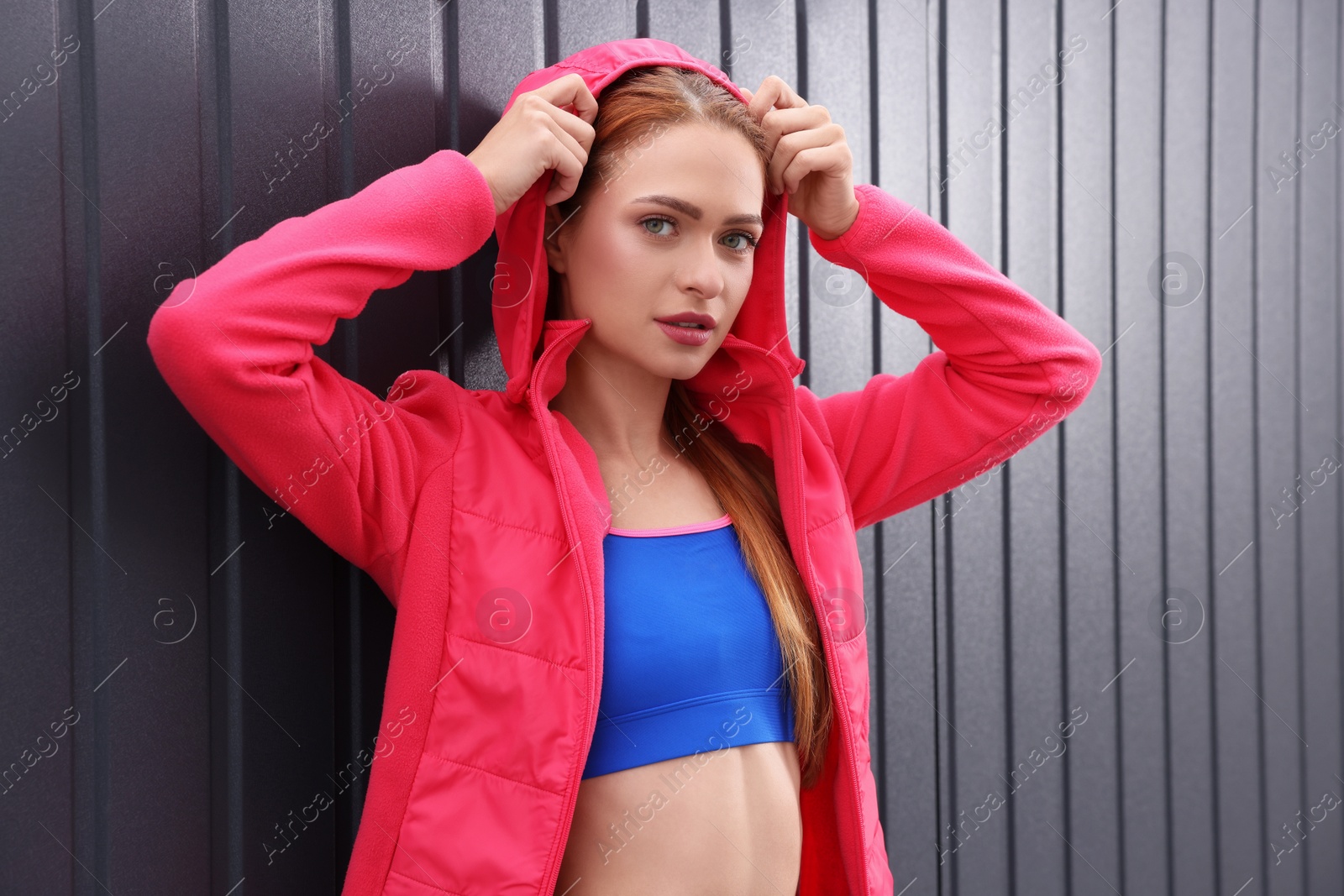 Photo of Beautiful woman in gym clothes posing near dark grey wall on street