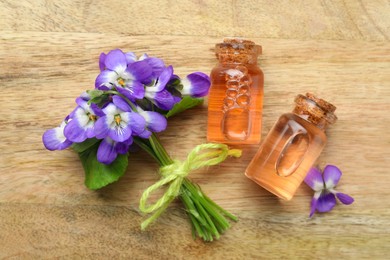 Photo of Beautiful wild violets and essential oil on wooden table, flat lay. Spring flowers