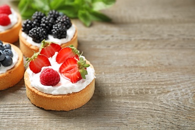 Photo of Different berry tarts on wooden table, space for text. Delicious pastries