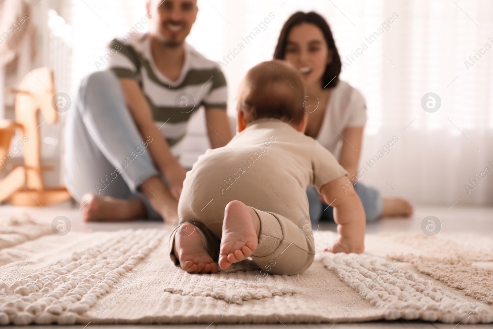 Photo of Happy parents watching their cute baby crawl on floor at home