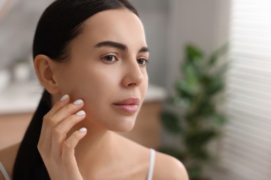 Woman with dry skin checking her face near mirror indoors, space for text