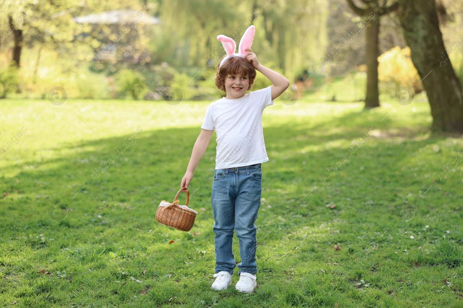 Photo of Easter celebration. Cute little boy in bunny ears holding wicker basket outdoors