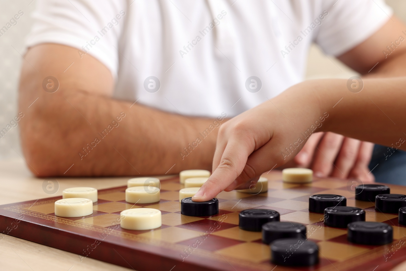 Photo of Father playing checkers with his son at table in room, closeup