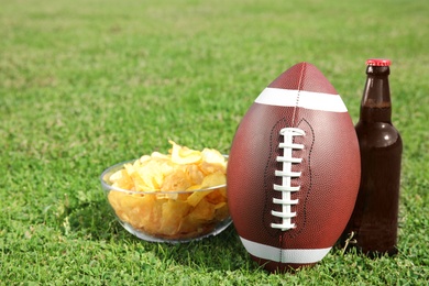 Photo of Ball with beverage and chips on fresh green field grass. American football match